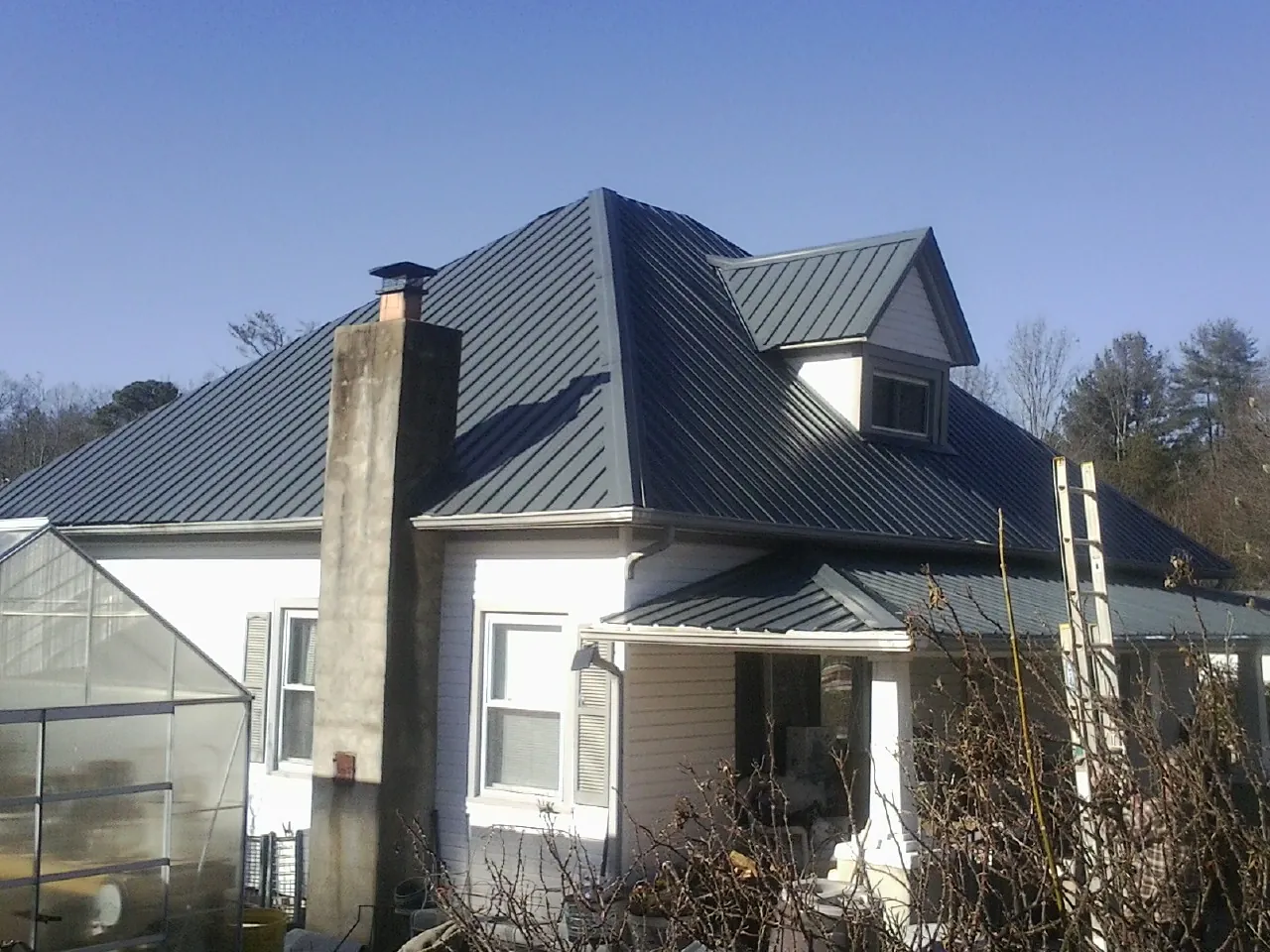 Dark blue standing seam metal roof on a white farmhouse with dormer — Slate & Tile Roof Repair by Roofing Brothers in Fort Lawn