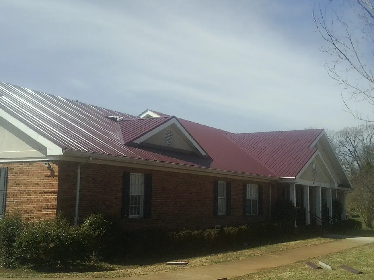 Red metal roof with gabled entries on a long brick building, from a Hail Damage Roof Repair job in Fort Lawn