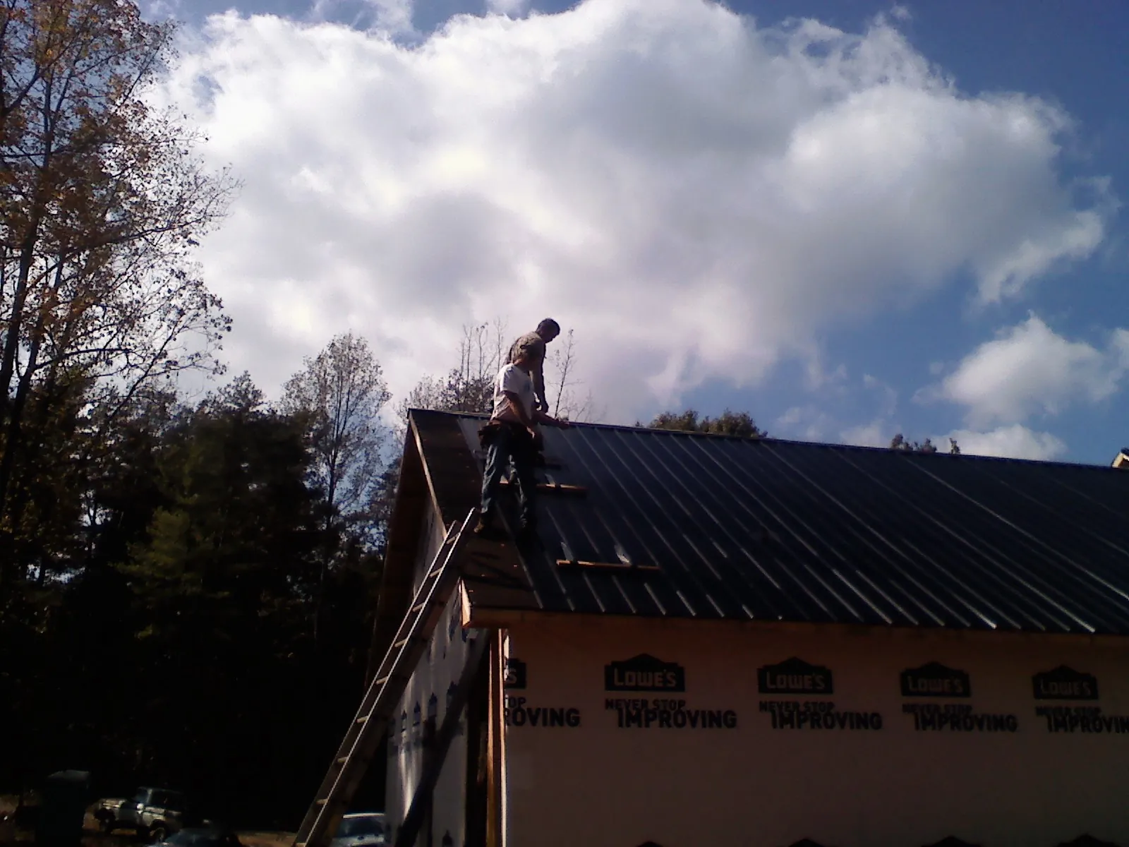 Roofer fastening dark metal panels high against a cloudy sky, from a Roof Inspection job in Fort Lawn
