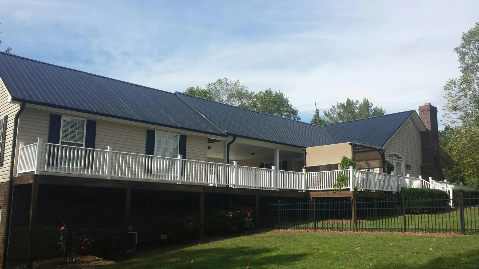Black metal roof above a long white railed deck on a hillside home in Fort Lawn