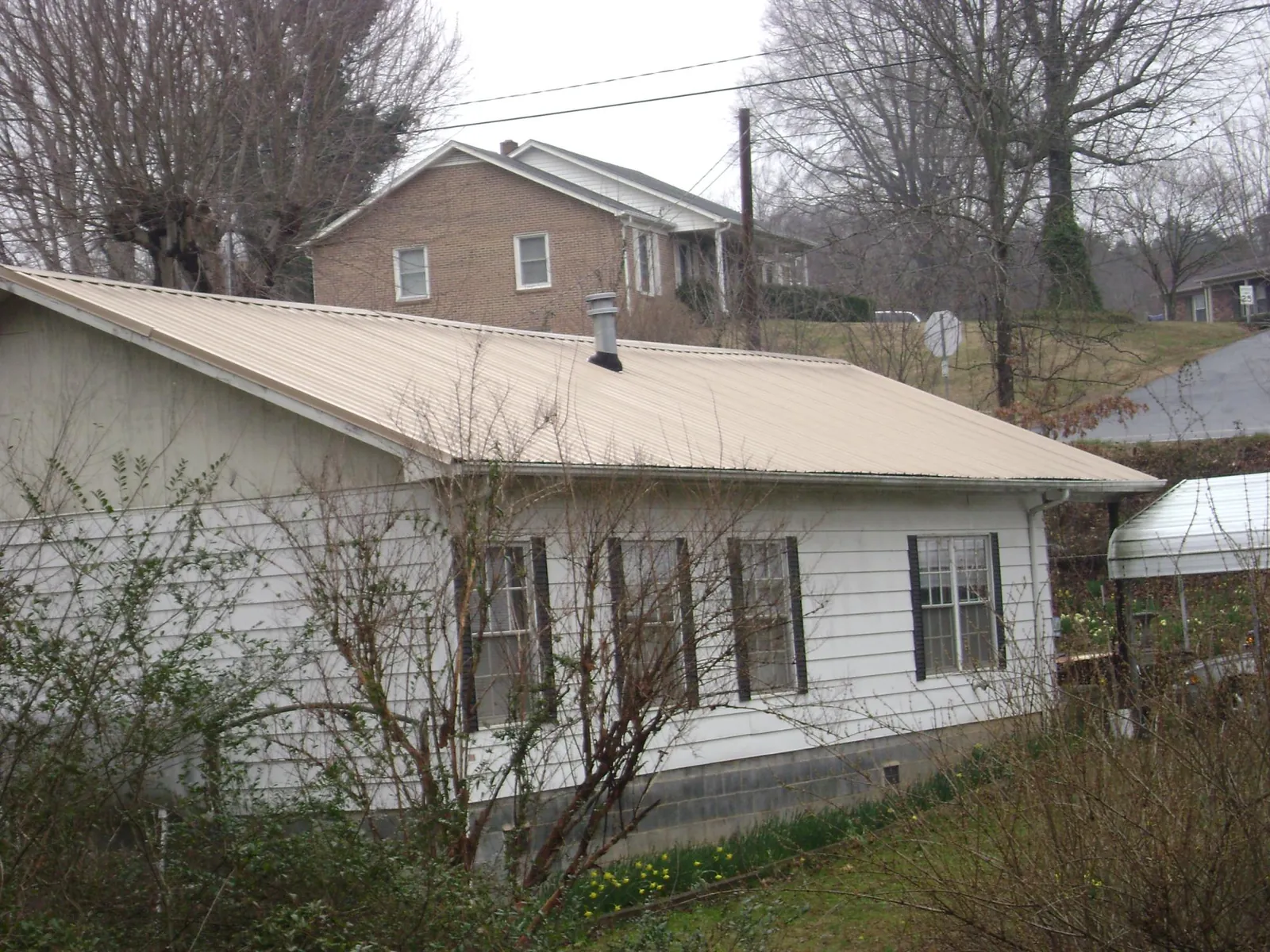 Tan metal roof on a white sided house set into a hillside — Commercial Roofing by Roofing Brothers in Fort Lawn
