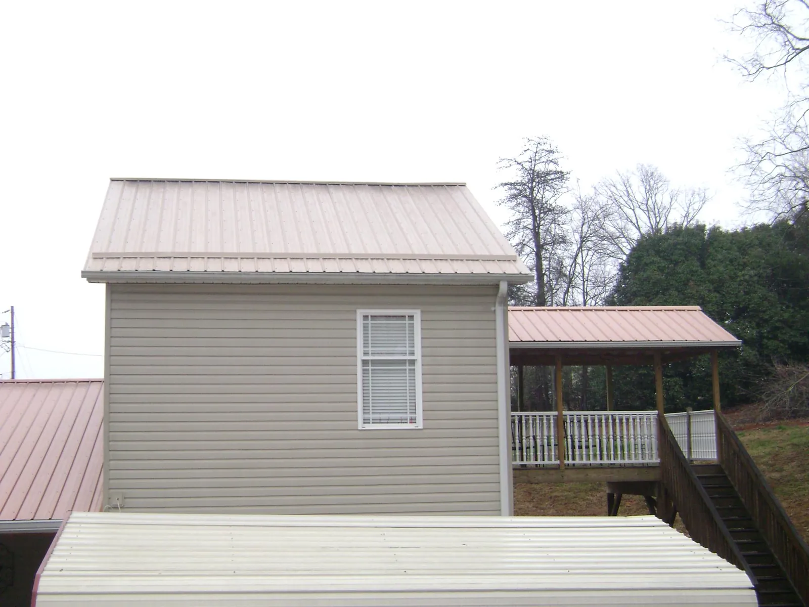 Tan metal roofs on a two story addition and attached porch, from a Roof Replacement job in Fort Lawn